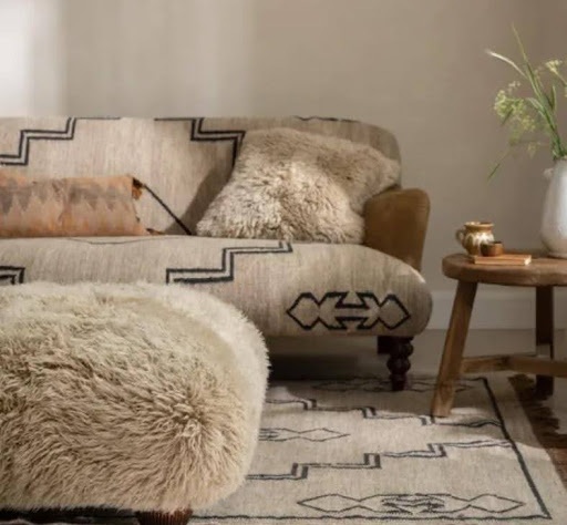 Neutral living room with a shaggy upholstered sofa, matching ottoman and patterned rug.