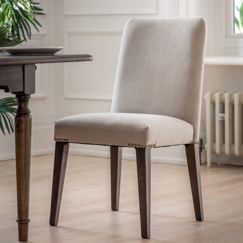 Gallery Direct Madison Dining Chair Cement Linen beside wooden dining table, grey linen upholstery with metal stud detailing