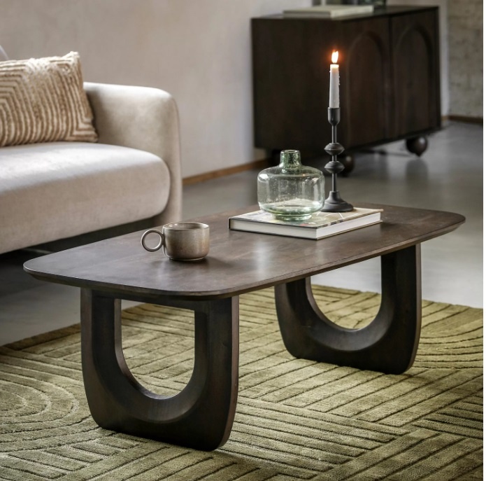 The Gallery Arc Coffee Table styled in a living room with rich mango wood grain and distinctive carved U-shaped leg design