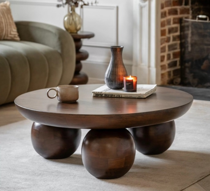 The Gallery Sculpt Round Coffee Table styled in a living room with rich mango wood finish and bold rounded ball feet