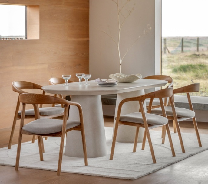 Modern linen-colored oval dining table styled in a minimalist dining room with wooden chairs.