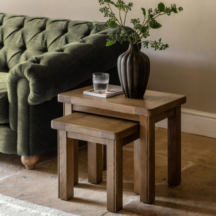 Gallery Direct Hardwick Nest of 2 Tables in oak finish, nested together in a living room setting with a green sofa.