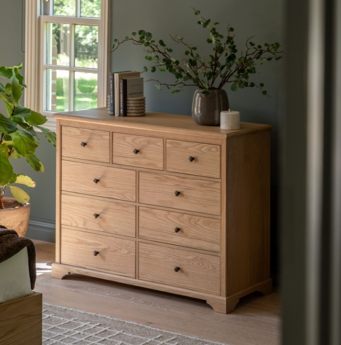 Gallery Direct Malvern 9 Drawer Chest next to window in bedroom with vase and flowers on top