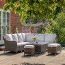 Gallery Garden Ascot corner dining set with rising table on a sunny stone patio with grey wicker and white cushions.