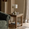 Gallery Direct Hardwick Side Table next to green sofa in corner with table lamp on top and glass of water